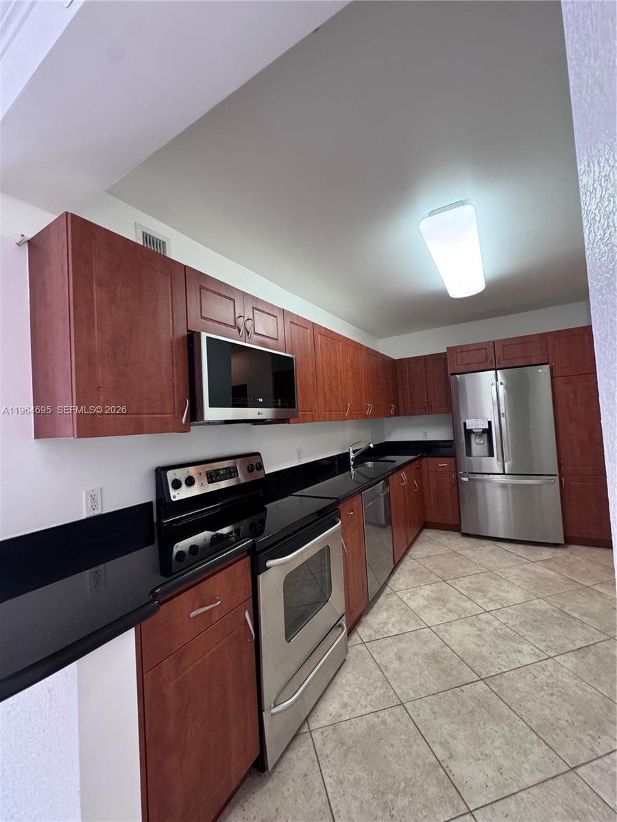 A kitchen features cherry wood cabinets, black countertops, stainless steel appliances, and tile flooring — 401 N 69th St # 607, Miami Beach FL 33141, MIAMI BEACH, FL
