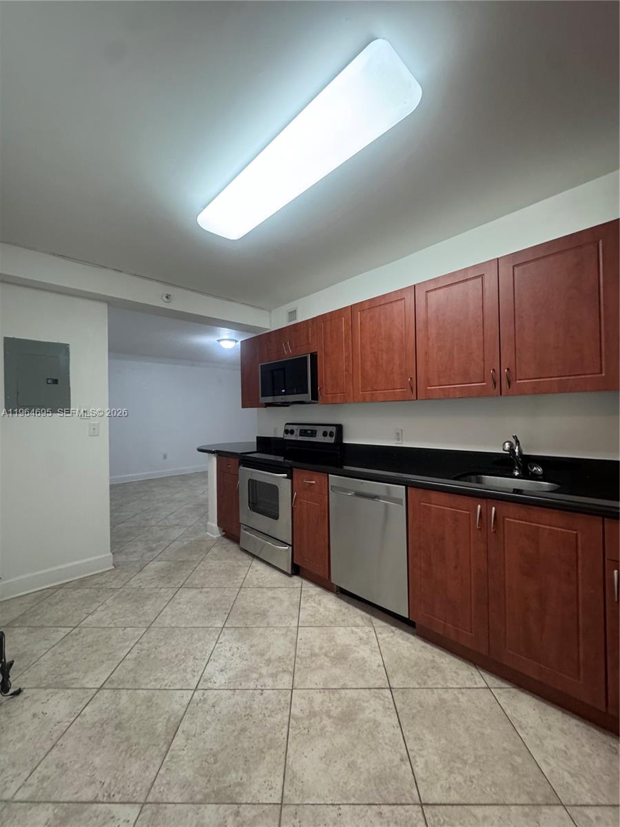 A kitchen features cherry wood cabinets, black countertops, stainless steel appliances, and light tile flooring — 401 N 69th St # 607, Miami Beach FL 33141, MIAMI BEACH, FL
