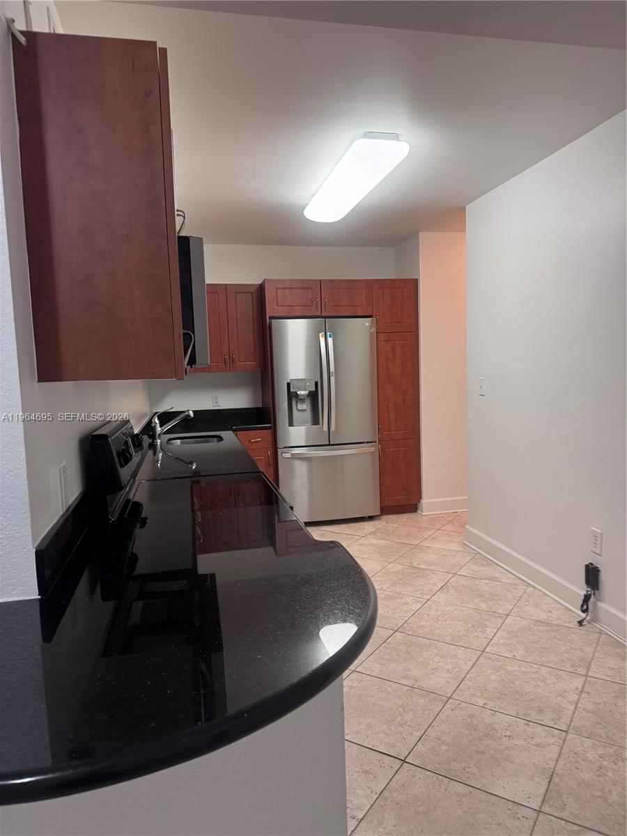 A kitchen features dark wood cabinets, black countertops, stainless steel appliances, and beige tile flooring — 401 N 69th St # 607, Miami Beach FL 33141, MIAMI BEACH, FL