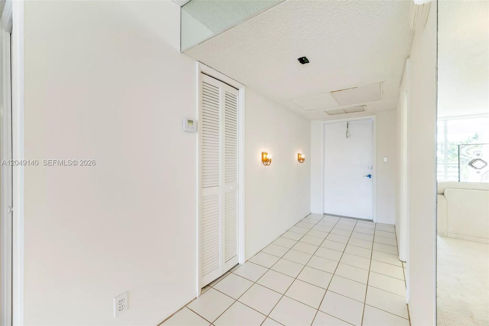 A tiled entryway features a white louvered closet door, wall sconces, and a white door — 605 Oaks Dr # 607, Pompano Beach FL 33069, POMPANO BEACH, FL
