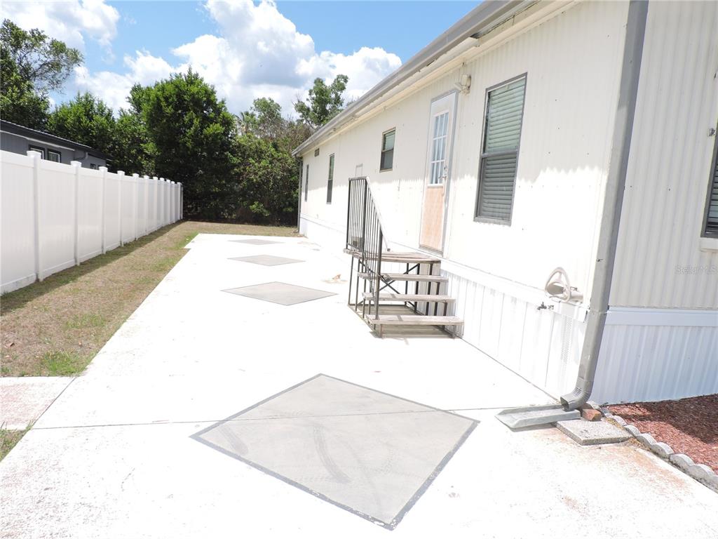 A white mobile home features a concrete patio with square insets and metal stairs — 236 2ND AVENUE N, LAKE WALES, FL