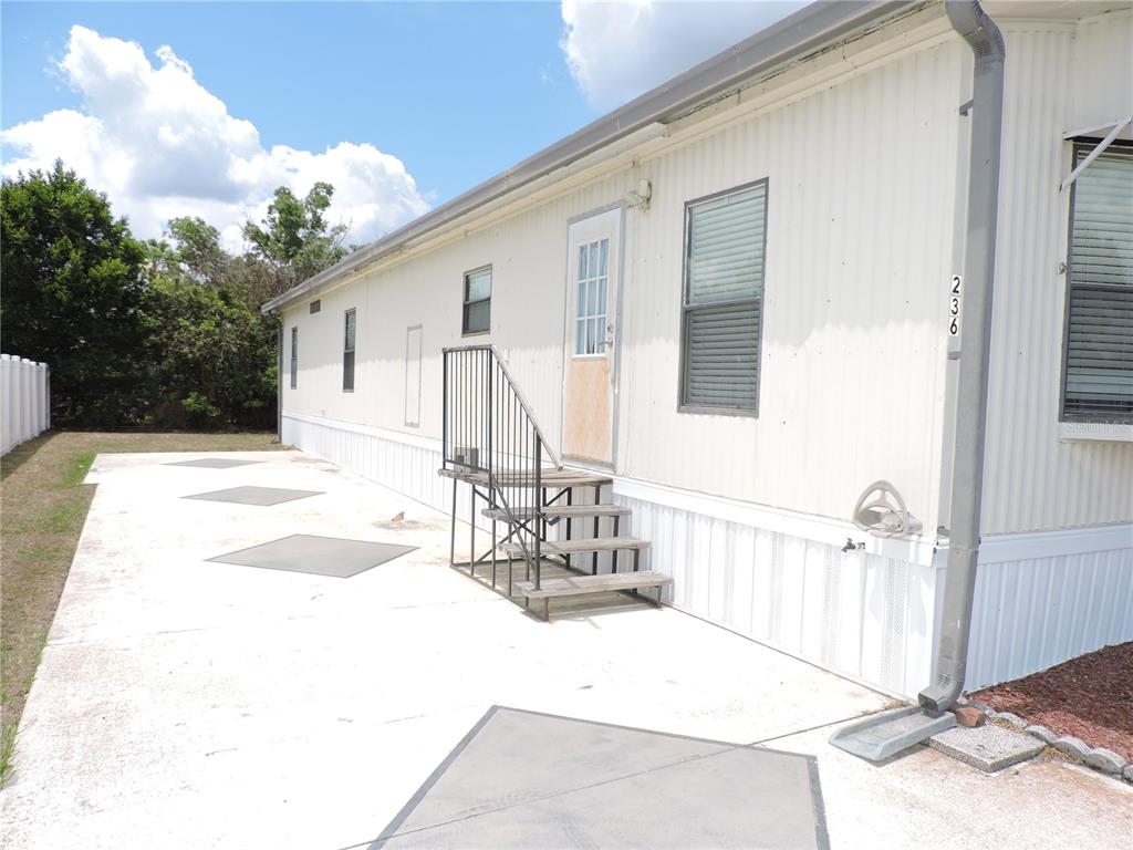 A side view of a mobile home with a concrete patio and metal stairs — 236 2ND AVENUE N, LAKE WALES, FL