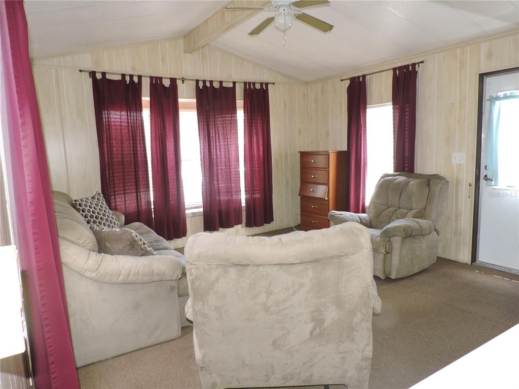 A living room features wood-paneled walls, a ceiling fan, beige carpet, and dark red curtains — 236 2ND AVENUE N, LAKE WALES, FL