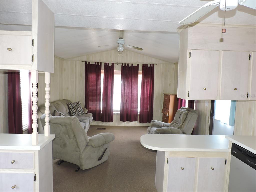 A living room with beige carpet, light wood-paneled walls, and maroon curtains over large windows — 236 2ND AVENUE N, LAKE WALES, FL
