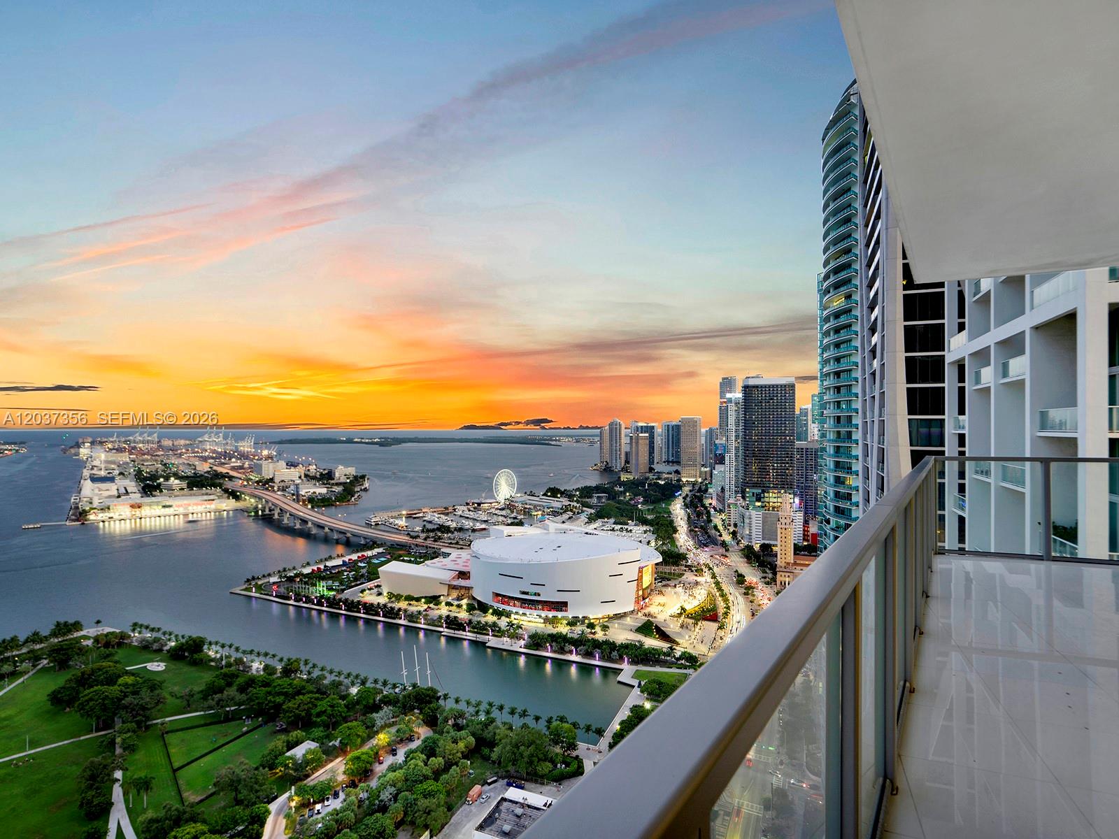 A high-angle view from a balcony overlooking a city skyline, harbor, and sunset — 1100 Biscayne Blvd # 4001, Miami FL 33132, MIAMI, FL