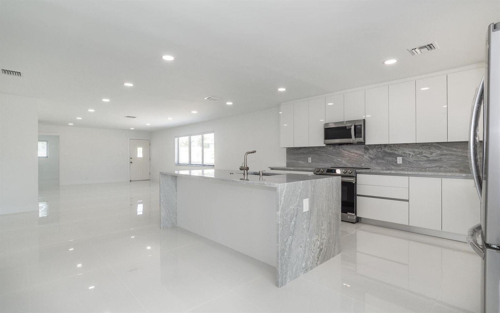 A modern kitchen features a marble waterfall island, white cabinetry, and glossy tile flooring — 524 NW 53rd Street, Boca Raton FL 33487, BOCA RATON, FL