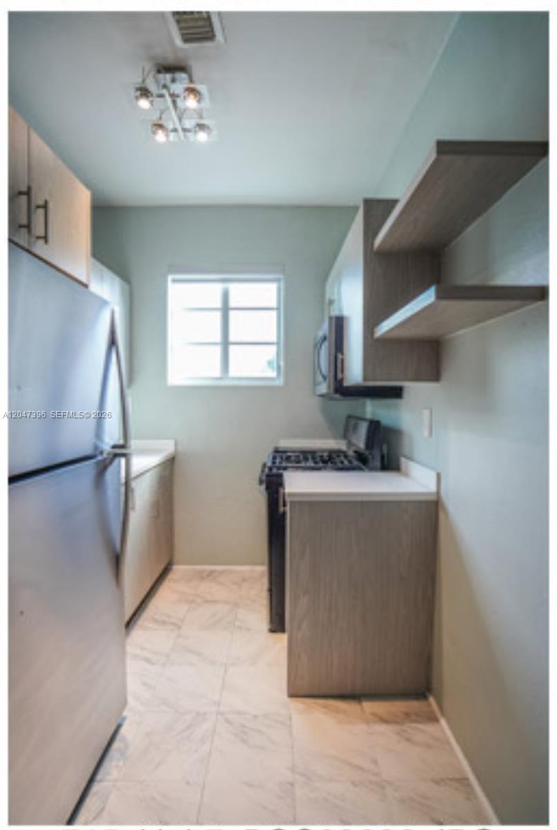 A galley kitchen features stainless steel appliances, light wood cabinets, open shelving, and marble-look flooring — 715 Michigan Ave # 7, Miami Beach FL 33139, MIAMI BEACH, FL