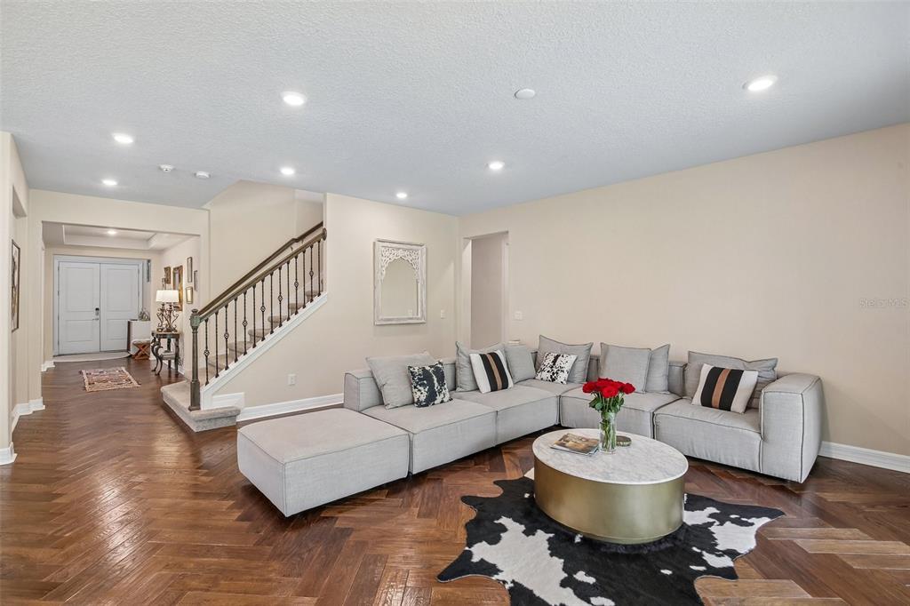 A living room features a large sectional sofa, a coffee table, and herringbone wood floors — 11054 SUNDRIFT DRIVE, TAMPA, FL