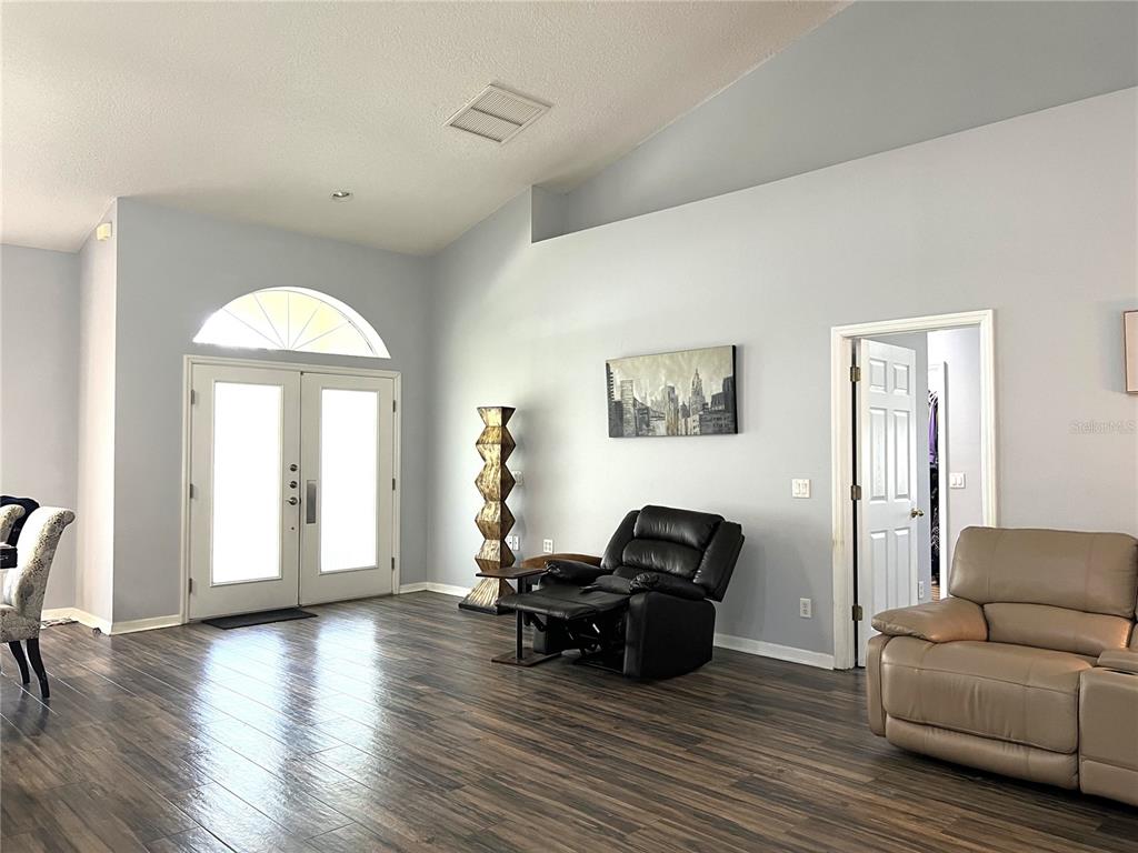 A living room features light blue walls, dark wood-look flooring, double entry doors, and furniture — 36320 PINEY RIDGE BOULEVARD, FRUITLAND PARK, FL