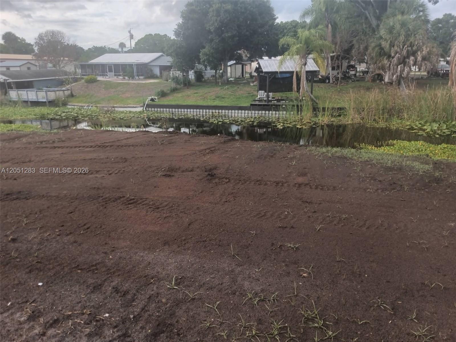 A cleared dirt lot overlooks a small canal with a dock and neighboring houses — 3707 SE 27th St, Okeechobee FL 34974, OKEECHOBEE, FL