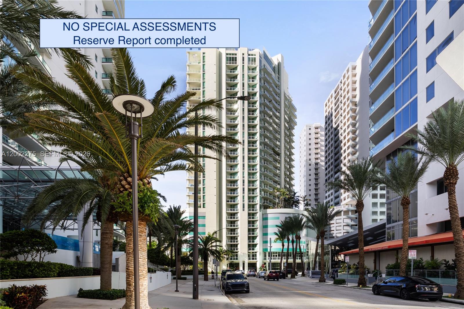 A street-level view of a tall, modern residential high-rise building surrounded by palm trees — 218 SE 14th St # 2105, Miami FL 33131, MIAMI, FL