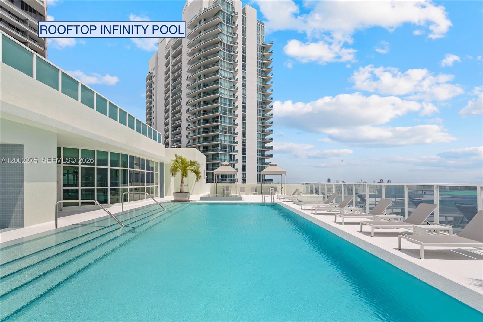 A rooftop infinity pool with lounge chairs and a tall residential building in the background — 218 SE 14th St # 2105, Miami FL 33131, MIAMI, FL