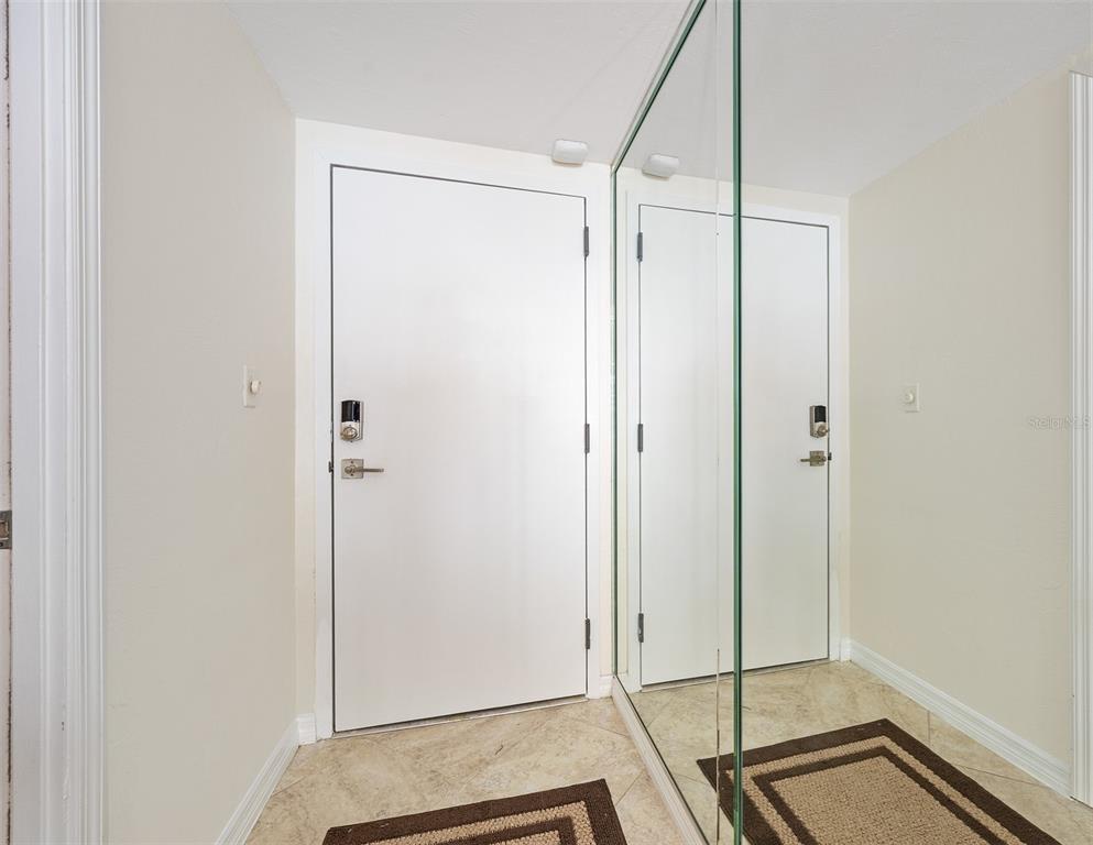 A white door with a smart lock stands next to a large floor-to-ceiling mirror — 2900 N ATLANTIC AVENUE UNIT 1501, DAYTONA BEACH, FL