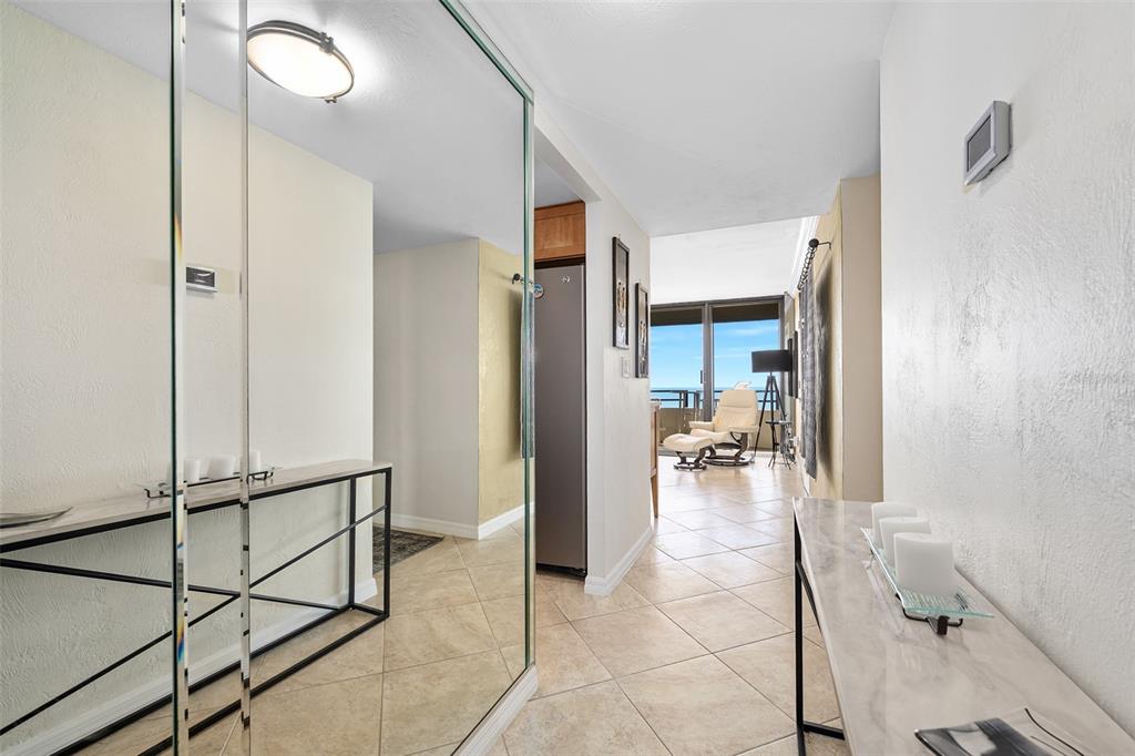 A tiled hallway leads past a mirrored wall and console table toward a sunlit living area — 2900 N ATLANTIC AVENUE UNIT 1501, DAYTONA BEACH, FL