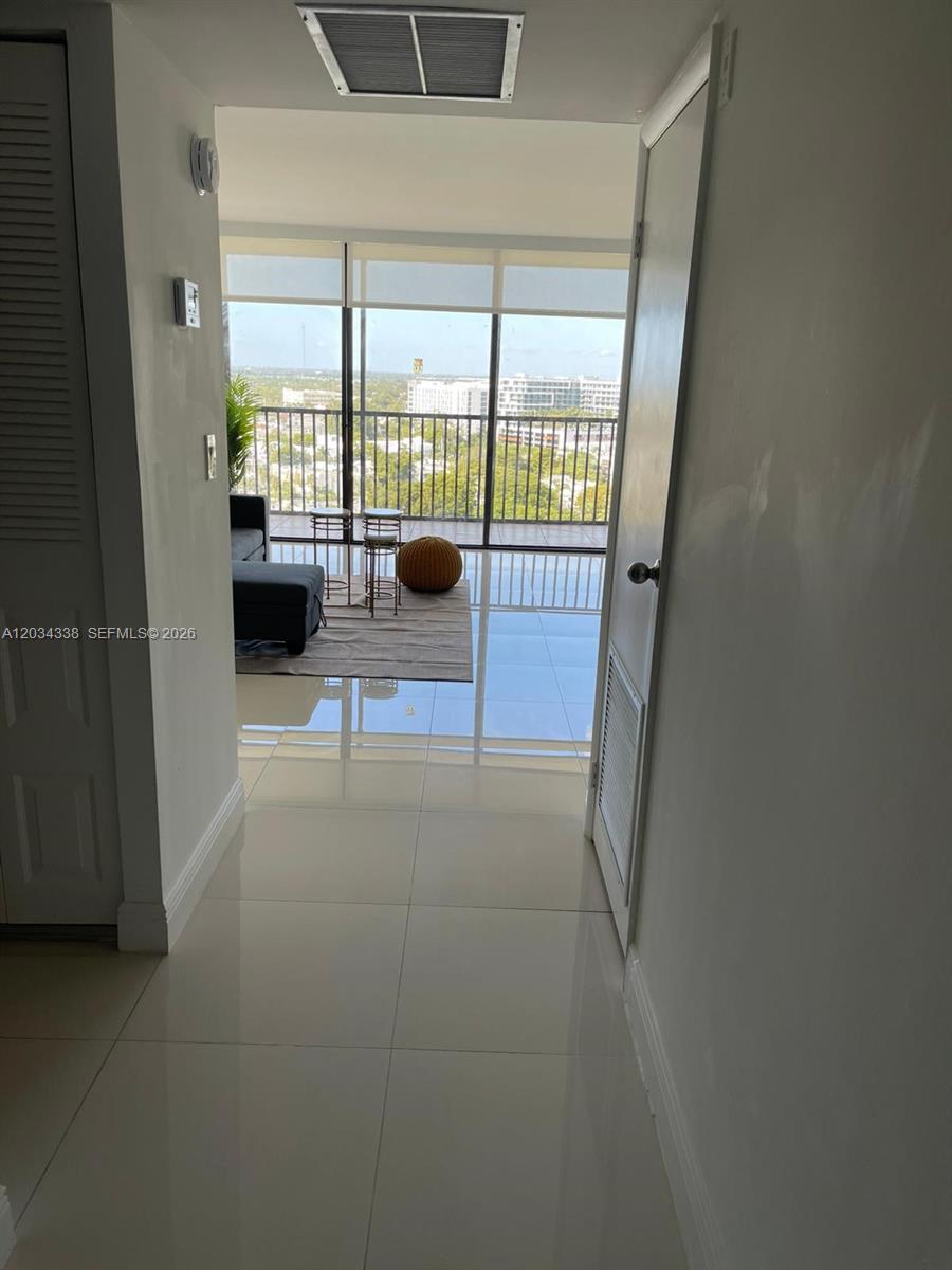 A hallway with white tile floors leads to a living room with floor-to-ceiling windows — AVENTURA, FL