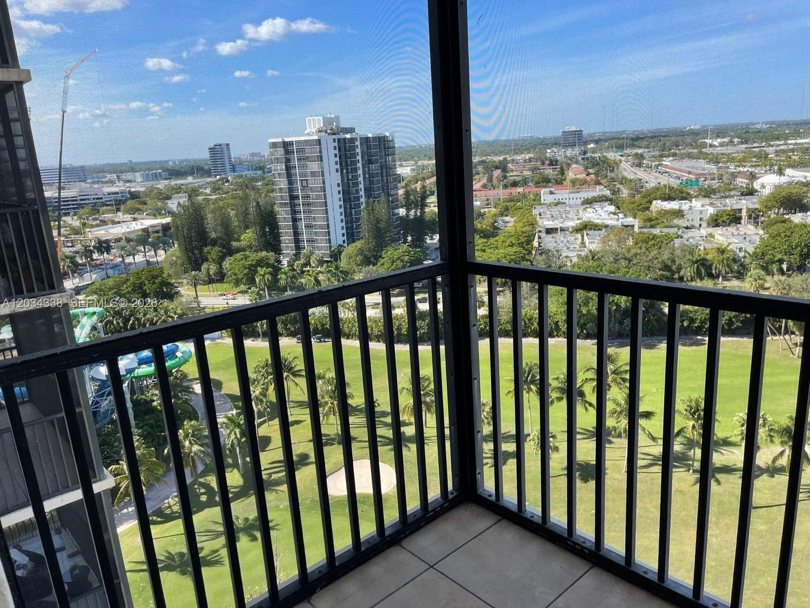 A screened balcony overlooks a golf course, palm trees, and distant high-rise buildings — AVENTURA, FL