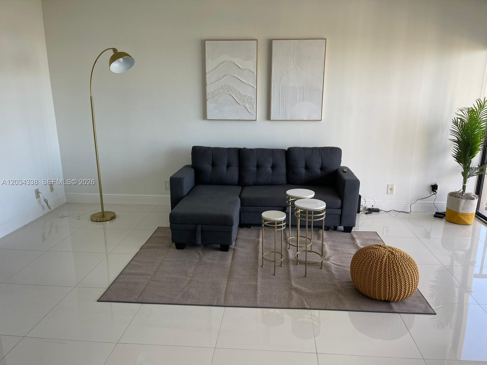 A living room features a dark gray sectional sofa, a rug, and gold-toned accent furniture — AVENTURA, FL