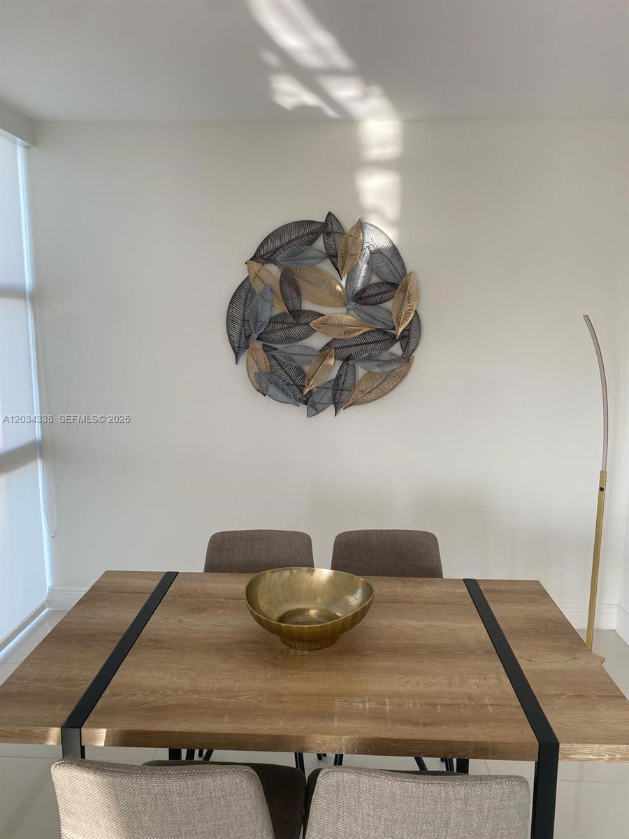 A dining room features a wooden table, four chairs, and a circular leaf-themed wall sculpture — AVENTURA, FL