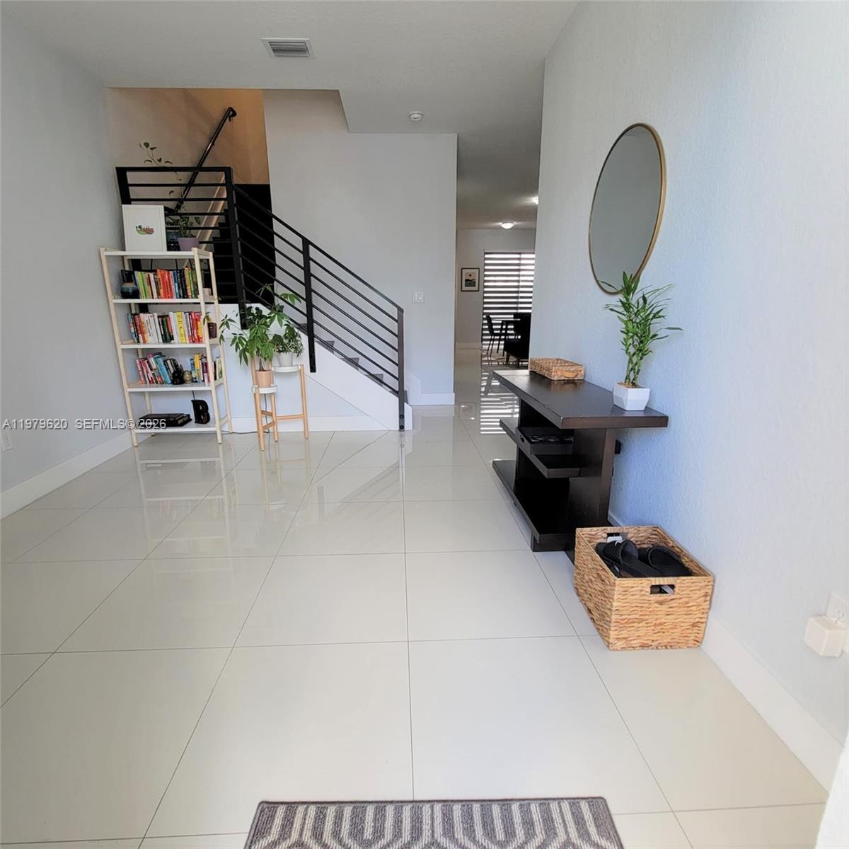 A bright entryway features white tile floors, a staircase with black railings, and minimalist furniture — 491 SW 91st Pl, Miami FL 33174, MIAMI, FL