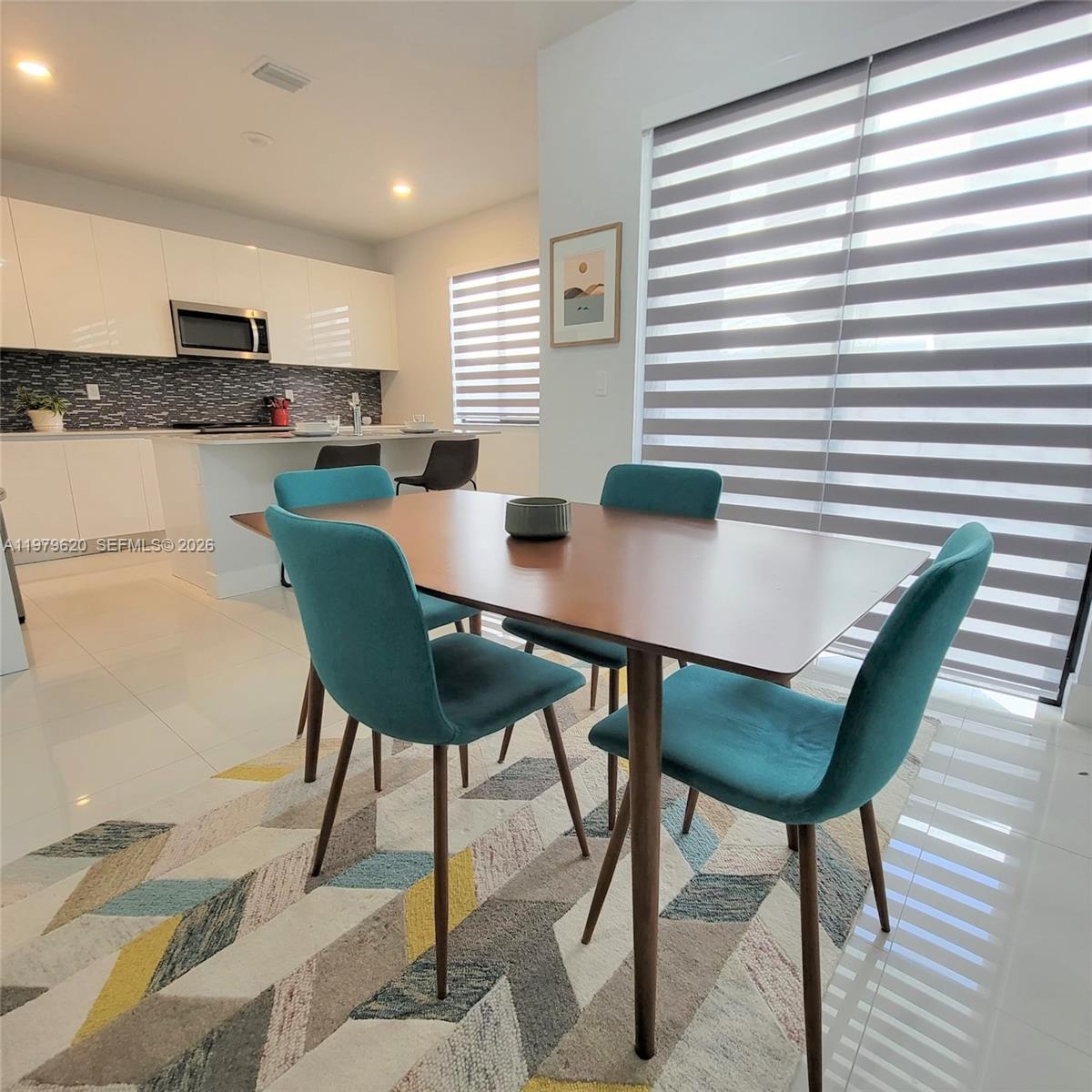 A dining area with a wooden table and teal chairs sits before a modern kitchen — 491 SW 91st Pl, Miami FL 33174, MIAMI, FL