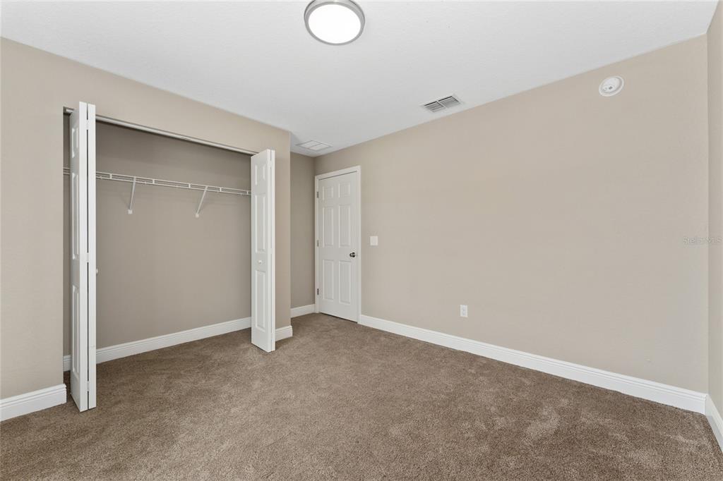 An empty bedroom features beige walls, brown carpeting, a white closet, and a white door — 146 JUNIPER WAY, OCALA, FL
