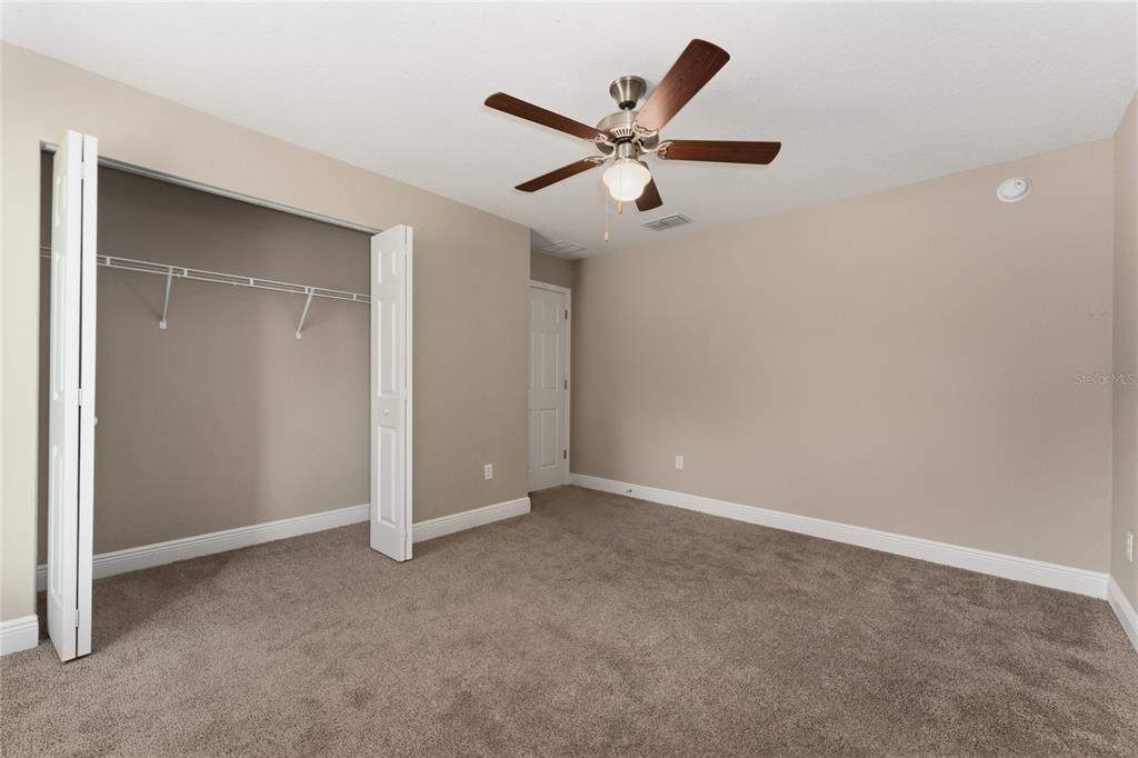 An empty bedroom features beige walls, brown carpet, a ceiling fan, and an open closet — 146 JUNIPER WAY, OCALA, FL