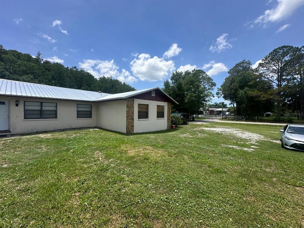 A single-story house with a metal roof and stone accents sits on a grassy lot — 17042 NATURE TRAIL, LUTZ, FL