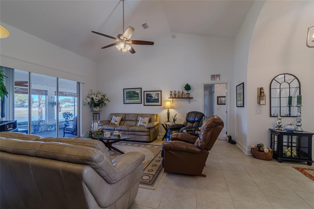 A living room with vaulted ceilings, tile floors, leather furniture, and a sliding glass door — 1956 NW 50TH CIRCLE, OCALA, FL