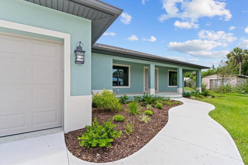 A light blue house exterior features a garage, a curved concrete walkway, and landscaped garden beds — 9171 PROSPECT AVENUE, ENGLEWOOD, FL