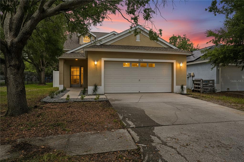 A tan single-story house with a two-car garage and a concrete driveway at sunset — 10215 LAKESIDE VISTA DRIVE, RIVERVIEW, FL
