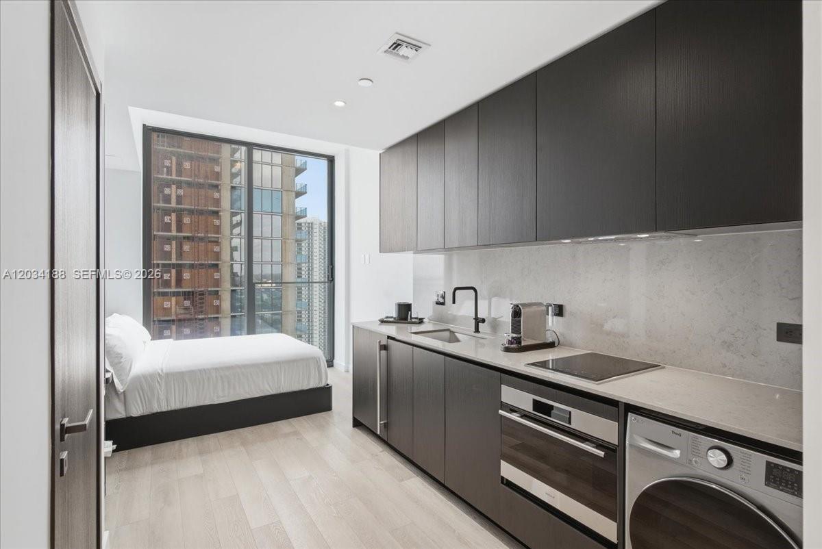 A modern studio apartment features a kitchenette with dark cabinets and an adjacent bed — 20 NE 11th # 4803, Miami FL 33132, MIAMI, FL