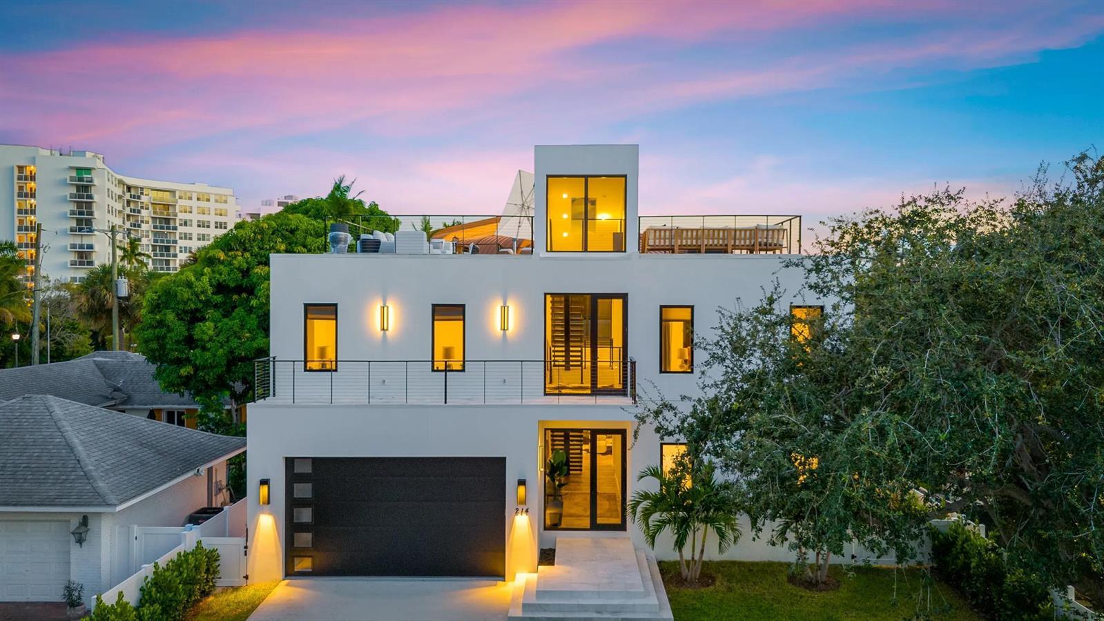 A modern three-story white house with a flat roof, balcony, and attached garage at dusk — 214 28th Street, West Palm Beach FL 33407, WEST PALM BEACH, FL