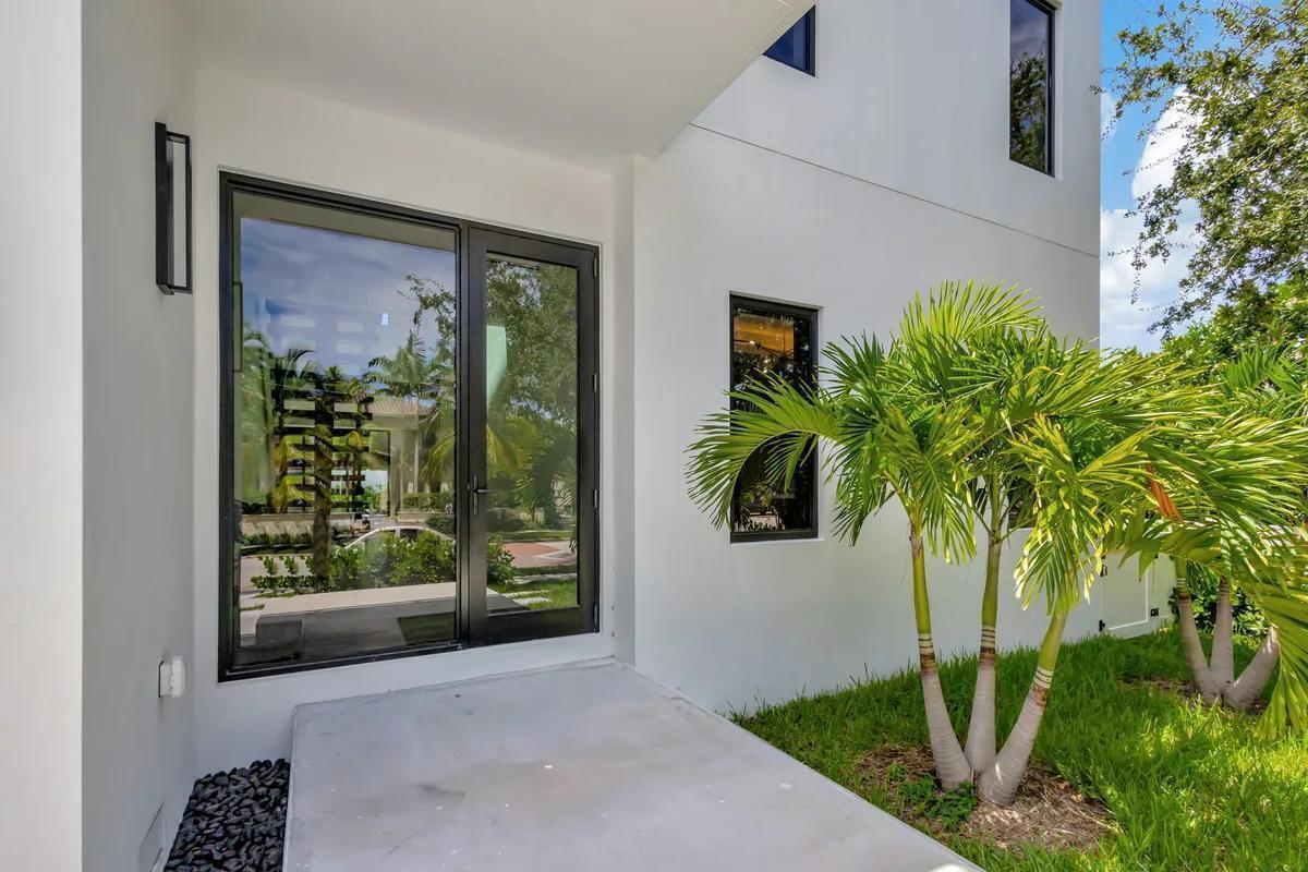 A modern white house exterior features a glass door, concrete porch, and small palm trees — 214 28th Street, West Palm Beach FL 33407, WEST PALM BEACH, FL