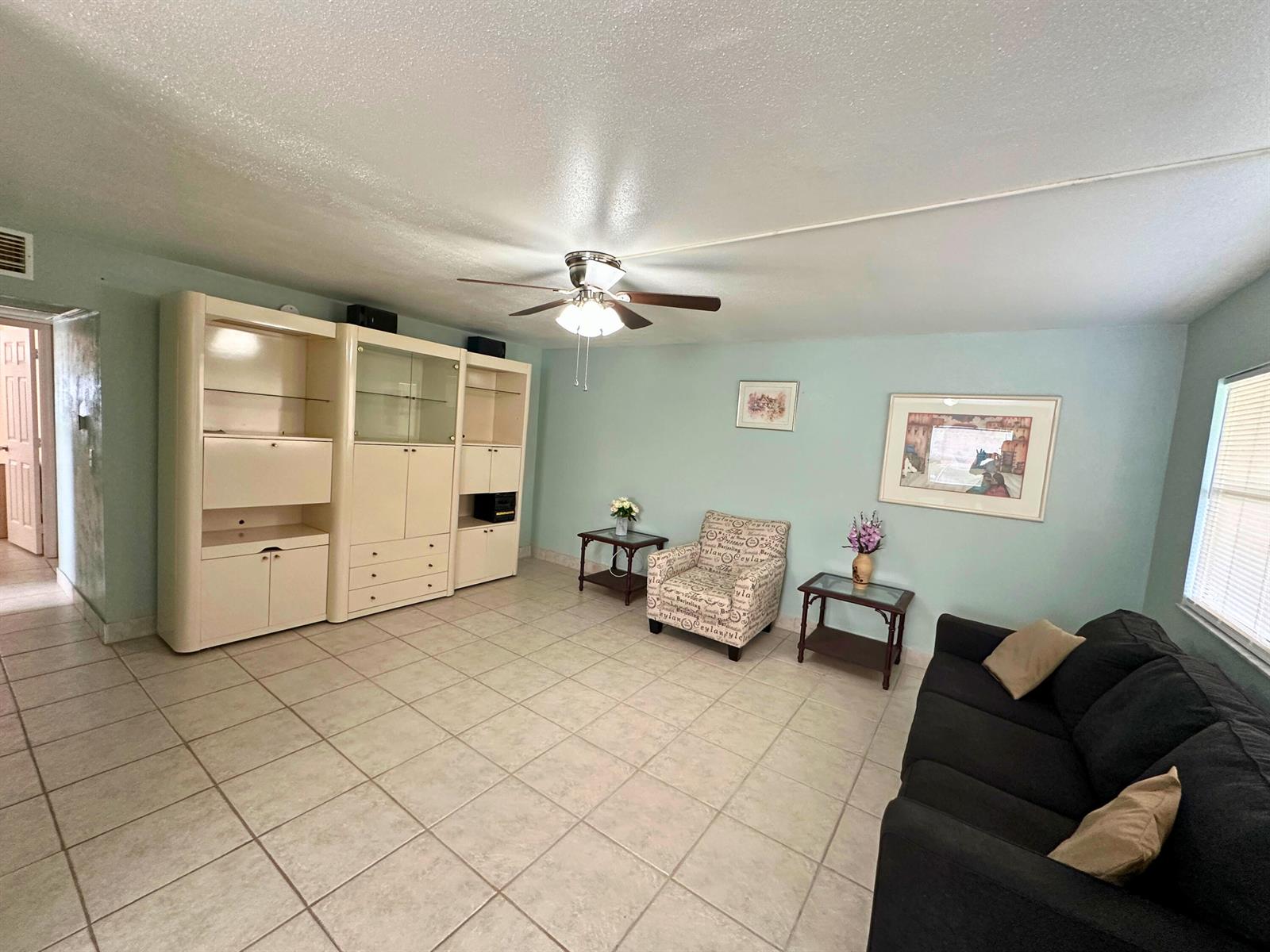A living room features light blue walls, tile flooring, a ceiling fan, and a large wall unit — 337 Saxony H Way # 337, Delray Beach FL 33446, DELRAY BEACH, FL