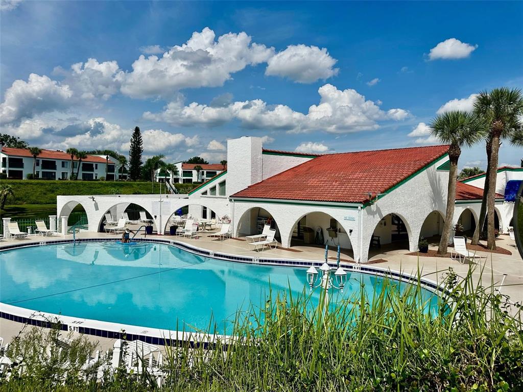A swimming pool sits in front of a white building with a red tile roof — 5435 CASABLANCA CIRCLE UNIT M22, SEBRING, FL