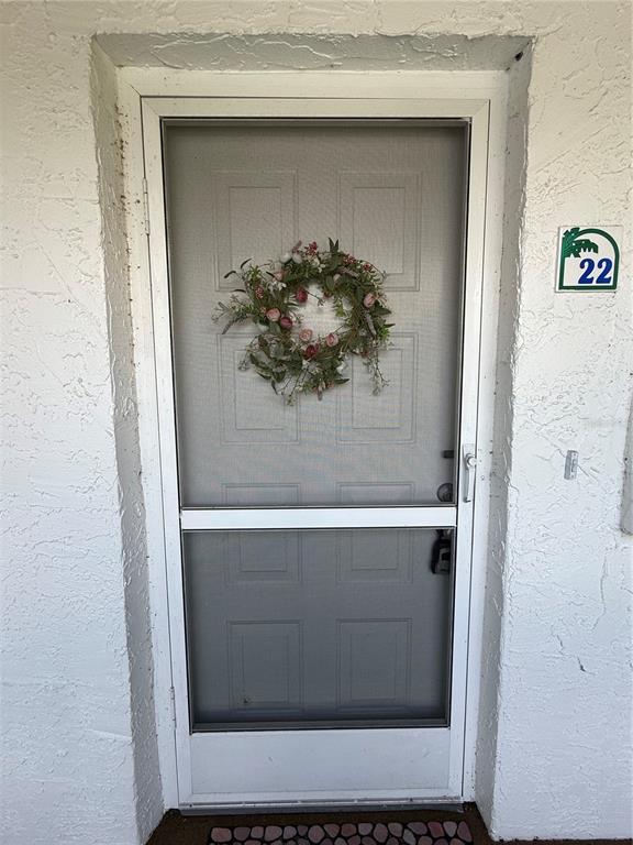 A white front door with a screen and a floral wreath is set in a wall — 5435 CASABLANCA CIRCLE UNIT M22, SEBRING, FL
