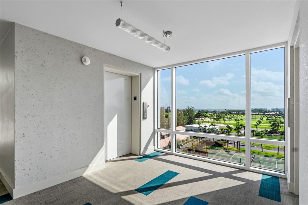 An elevator lobby with speckled walls, carpeted floors, and large windows overlooking a golf course — 2425 GULF OF MEXICO DRIVE UNIT 7C, LONGBOAT KEY, FL