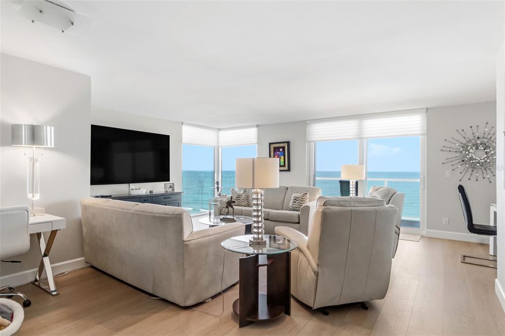A living room with light wood floors, neutral furniture, and floor-to-ceiling windows overlooking the ocean — 2425 GULF OF MEXICO DRIVE UNIT 7C, LONGBOAT KEY, FL