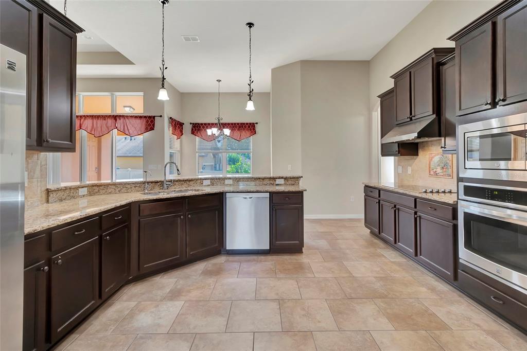 A kitchen with dark wood cabinets, granite countertops, stainless steel appliances, and tile flooring — 10816 WYANDOTTE DRIVE, CLERMONT, FL