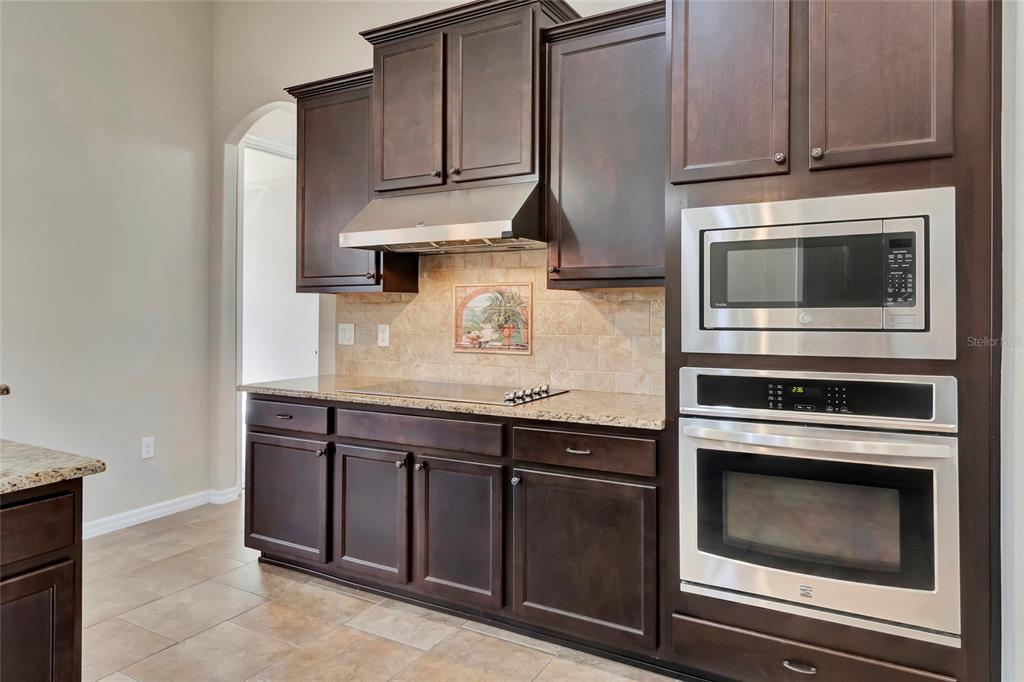 A kitchen features dark wood cabinets, stainless steel appliances, a tiled backsplash, and granite countertops — 10816 WYANDOTTE DRIVE, CLERMONT, FL