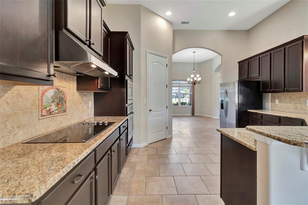 A kitchen with dark wood cabinets, granite countertops, stainless steel appliances, and tile flooring — 10816 WYANDOTTE DRIVE, CLERMONT, FL