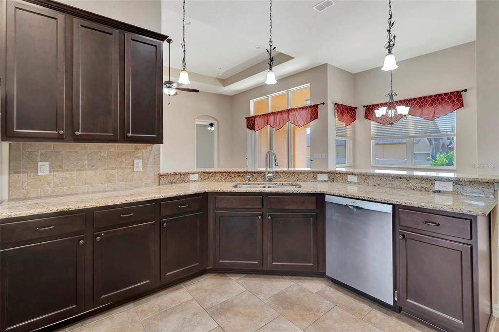 A kitchen features dark wood cabinets, granite countertops, a stainless steel dishwasher, and pendant lighting — 10816 WYANDOTTE DRIVE, CLERMONT, FL