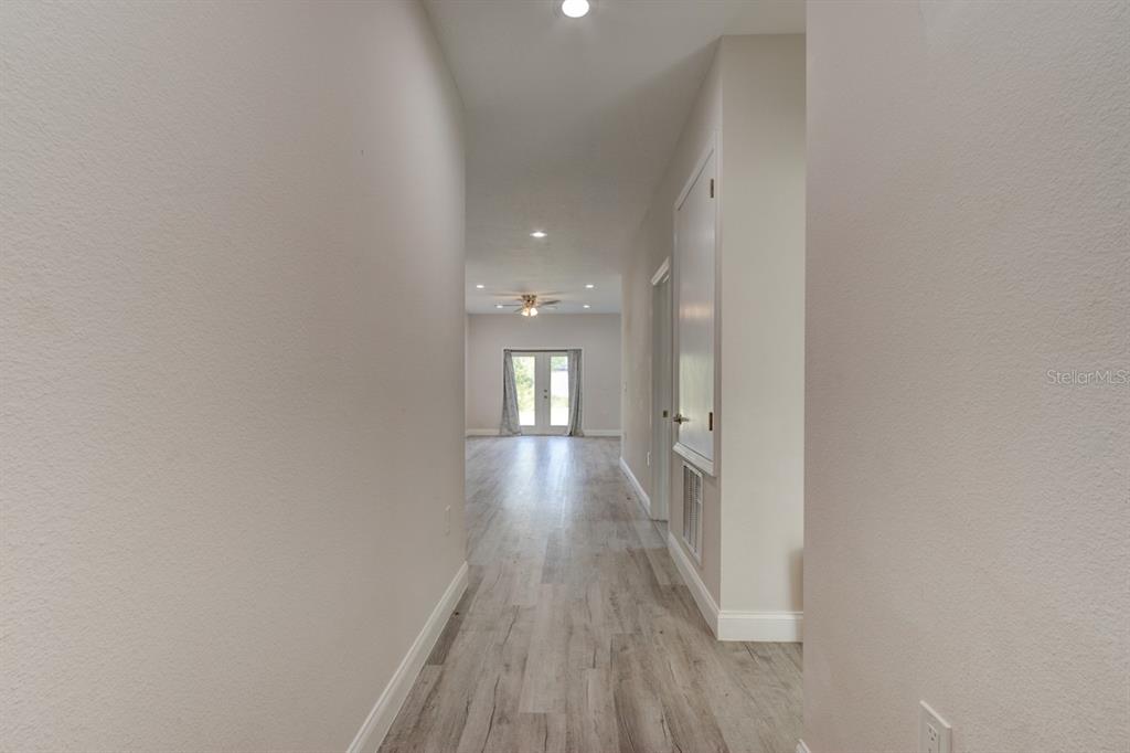 A hallway with light wood-look flooring leads toward a room with French doors — 1680 9TH AVENUE, DELAND, FL