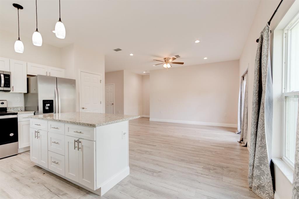 A kitchen with a granite-topped island and stainless steel appliances opens to a living area — 1680 9TH AVENUE, DELAND, FL