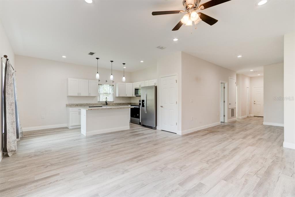 An open-concept kitchen and living area features white cabinetry, stainless steel appliances, and wood-look flooring — 1680 9TH AVENUE, DELAND, FL