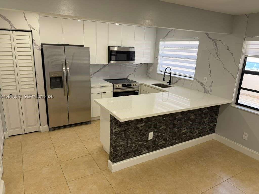 A kitchen features white cabinets, stainless steel appliances, a quartz countertop, and a stone-tiled island — 13470 SW 62nd St # 105N, Miami FL 33183, MIAMI, FL