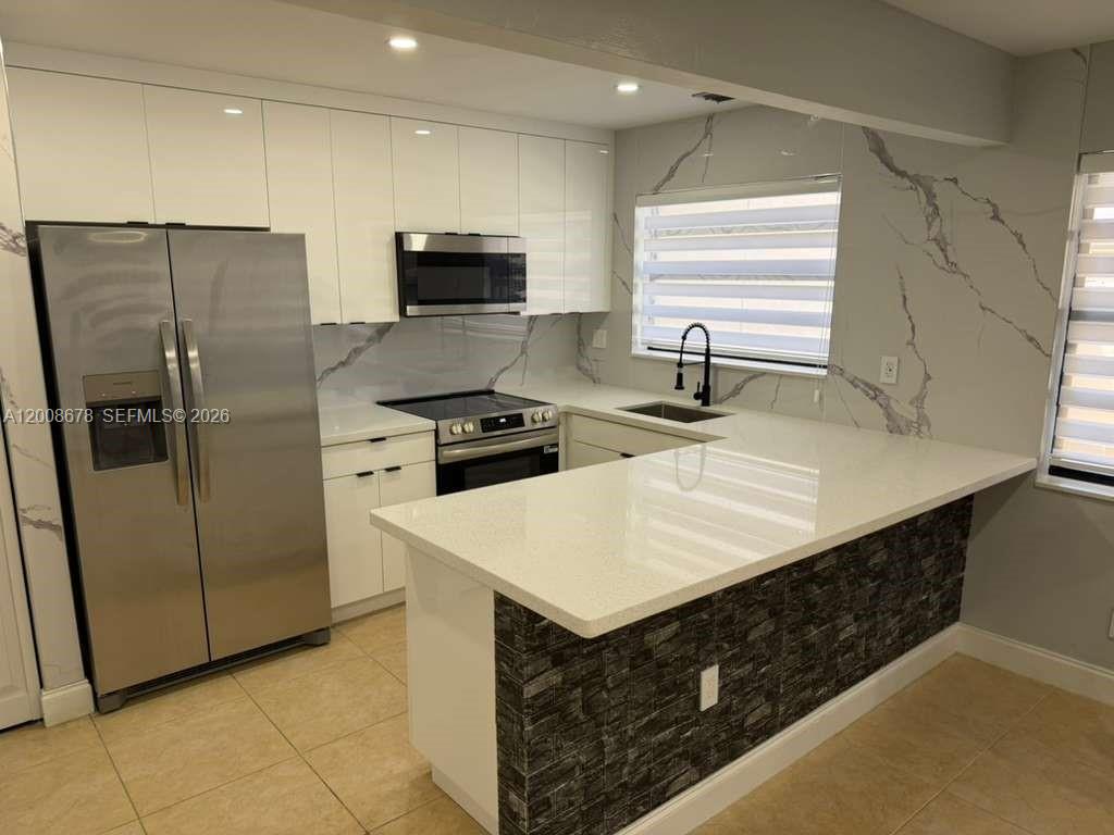 A modern kitchen features white cabinets, stainless steel appliances, and a stone-tiled breakfast bar — 13470 SW 62nd St # 105N, Miami FL 33183, MIAMI, FL