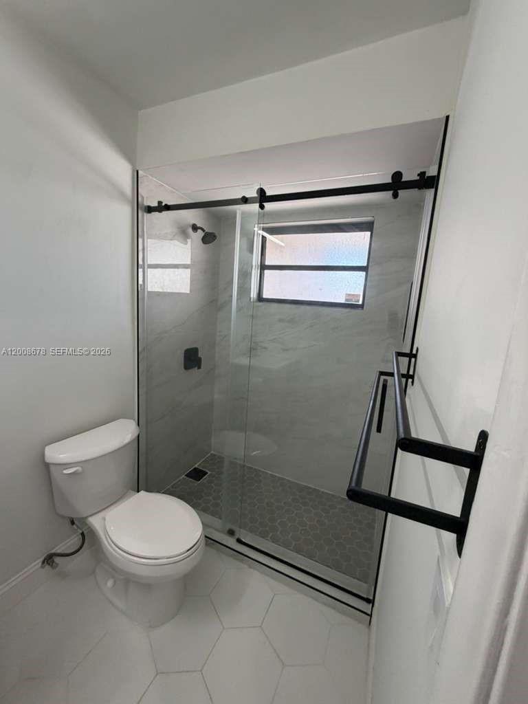A bathroom features a glass-enclosed shower with gray tile, a toilet, and white flooring — 13470 SW 62nd St # 105N, Miami FL 33183, MIAMI, FL