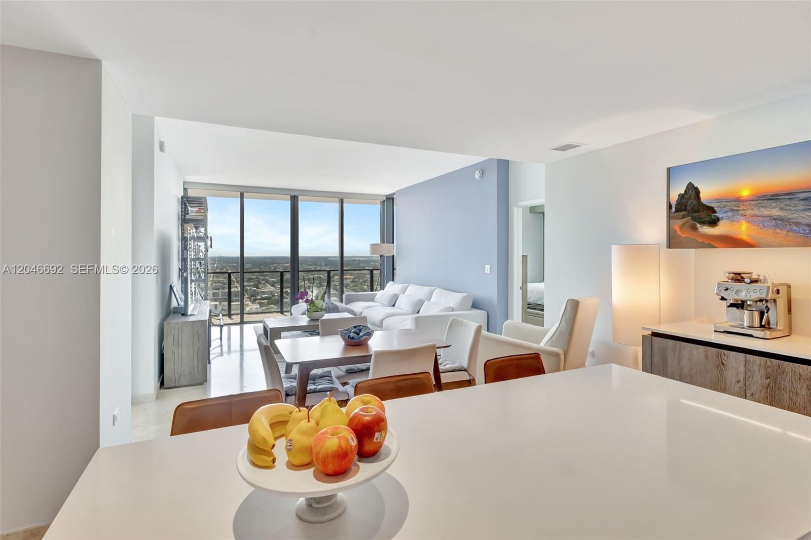 A white kitchen island with a fruit bowl overlooks a living area with floor-to-ceiling windows — 88 SW 7th St # 3604, Miami FL 33130, MIAMI, FL