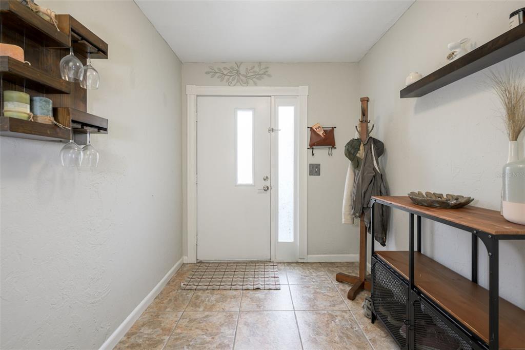 An entryway features a white front door, tiled flooring, a coat rack, and wall shelving — 21 OAKWOOD PARK, ORMOND BEACH, FL
